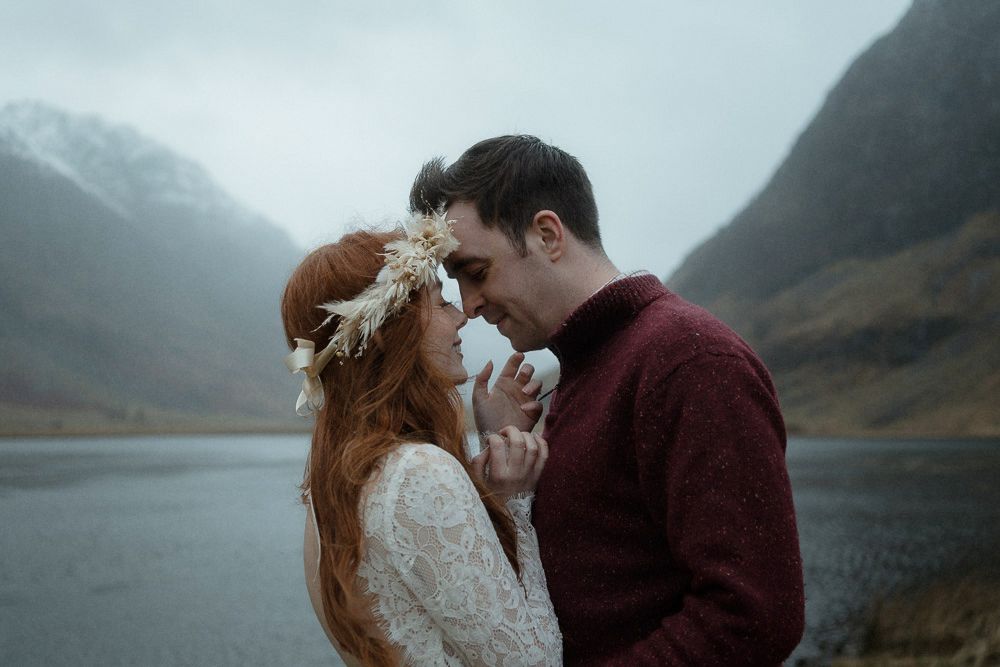 A bridge and groom get close and kiss by a huge loch on their wedding day in Glencoe, Scotland