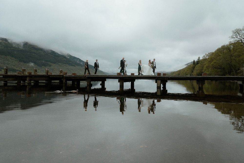 A bridal party walks across a bridge to their ceremony destination in Loch Lomond, Scotland