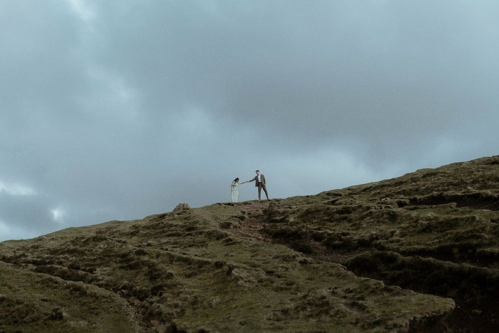 A bridge and groom climb a mountain before their elopement ceremony on the Isle of Skye, Scotland.