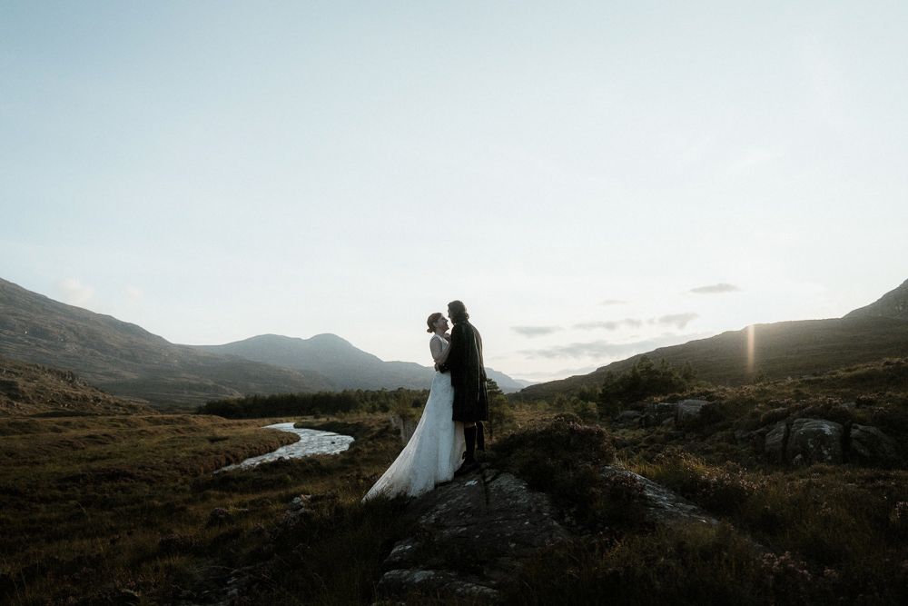 Couple stand on the banks of a river at sunset after their elopement near Torridon, Scotland