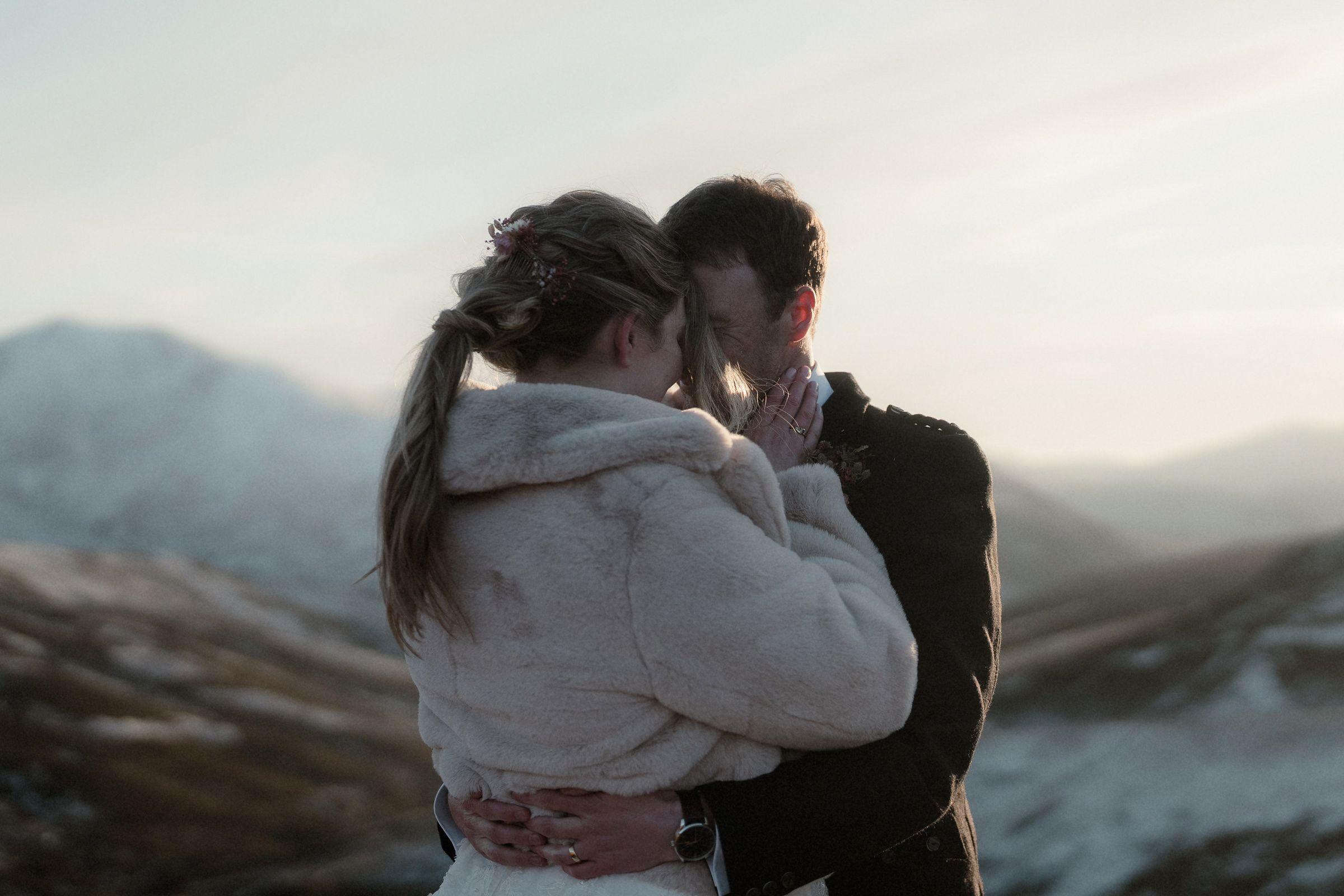 Bride and groom hold each other and kiss on a mountain at sunset after their elopement in the Cairngorms, Scotland
