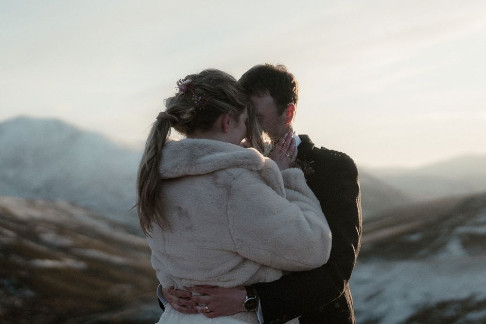 A couple hold each other and kiss on a mountain at sunset after their elopement in the Cairngorms, Scotland