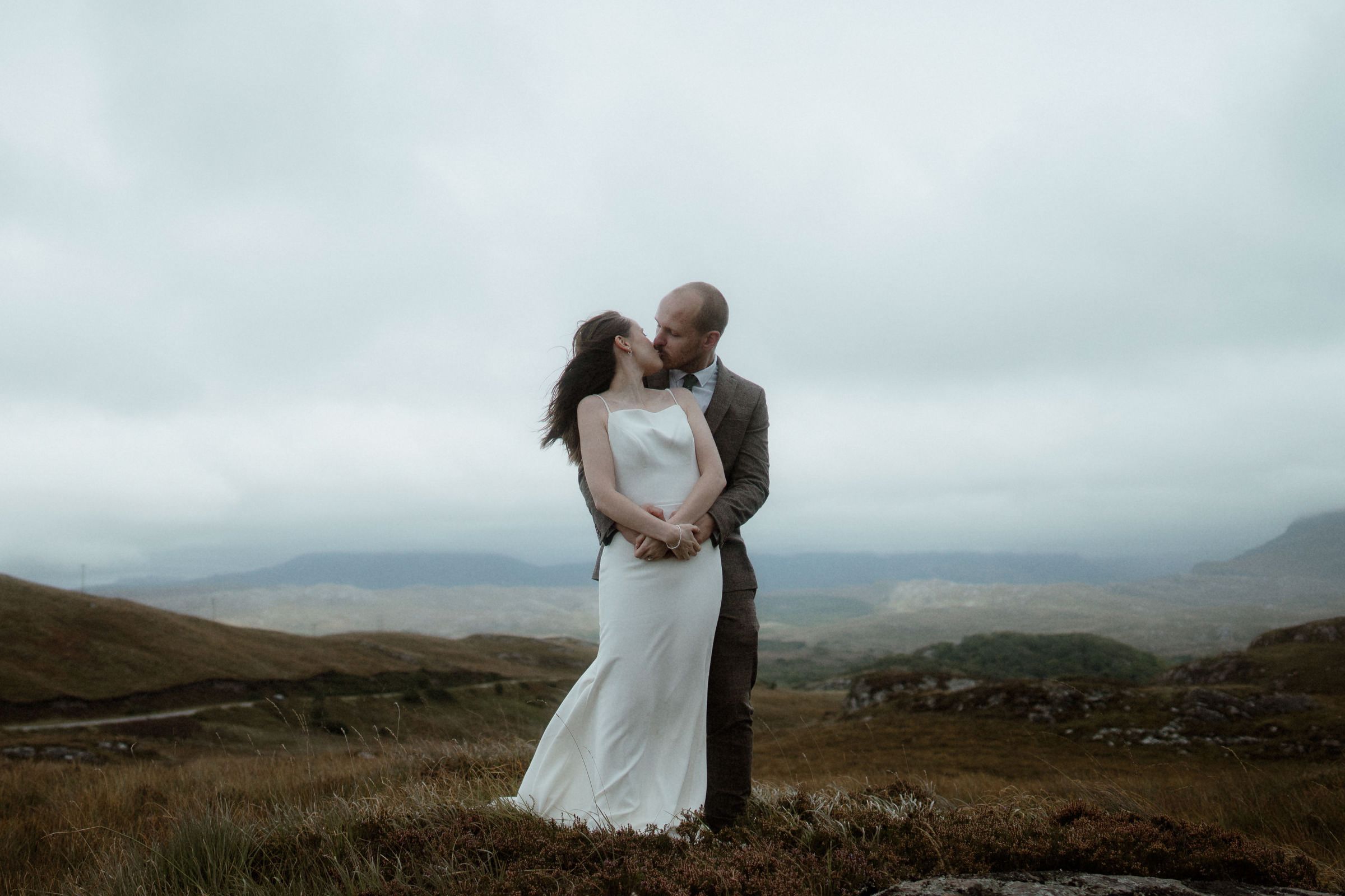 Bride and groom cuddle and embrace the wind after their Scottish elopement near Torridon in the Highlands