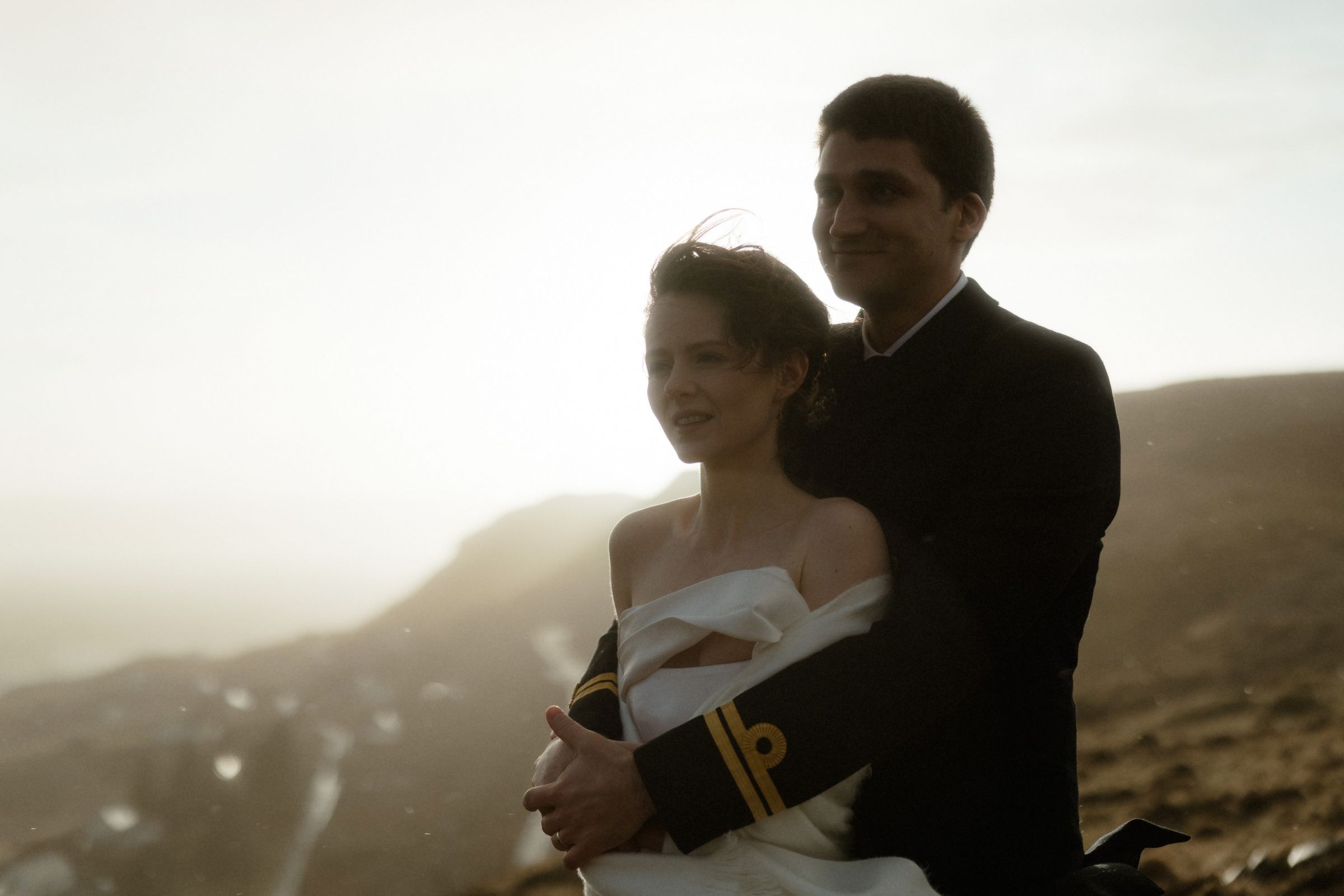A bride and groom hold each other tight during a sunset rain storm on the Isle of Skye, Scotland
