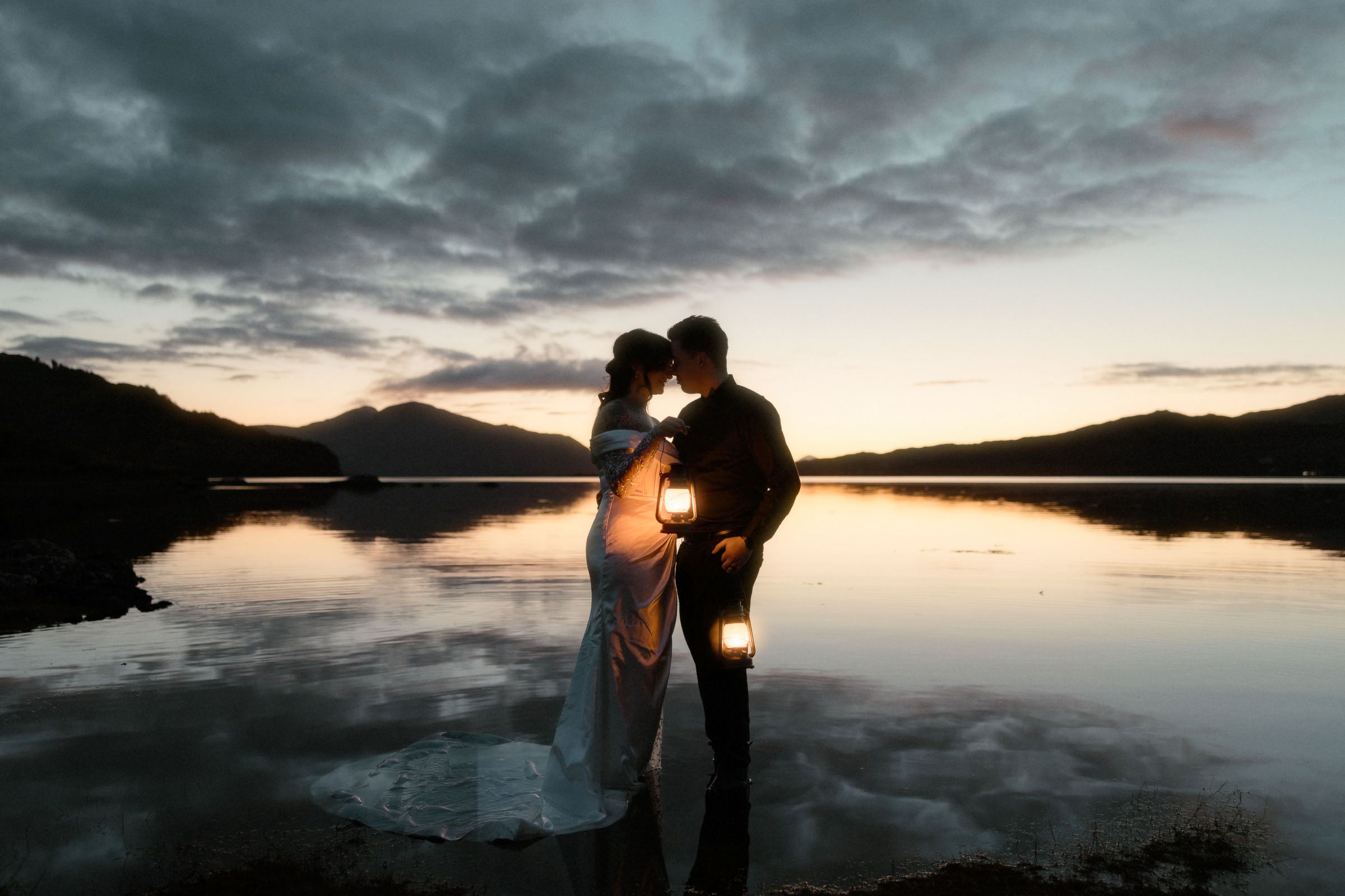 A bridge and groom stand in the shallow water of a Scottish loch at sunset during their elopement