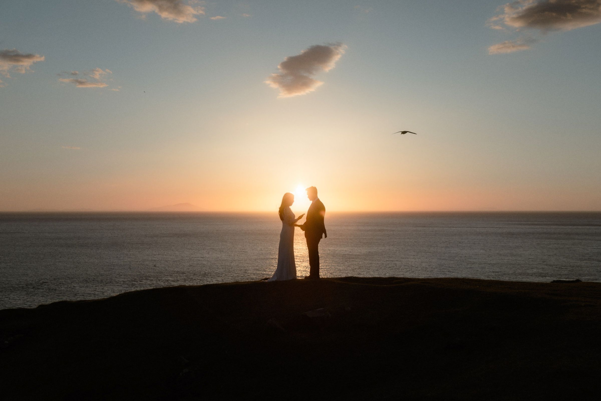 A couple make their vows in front of a beautiful sunset on their wedding day in the Highlands of Scotland