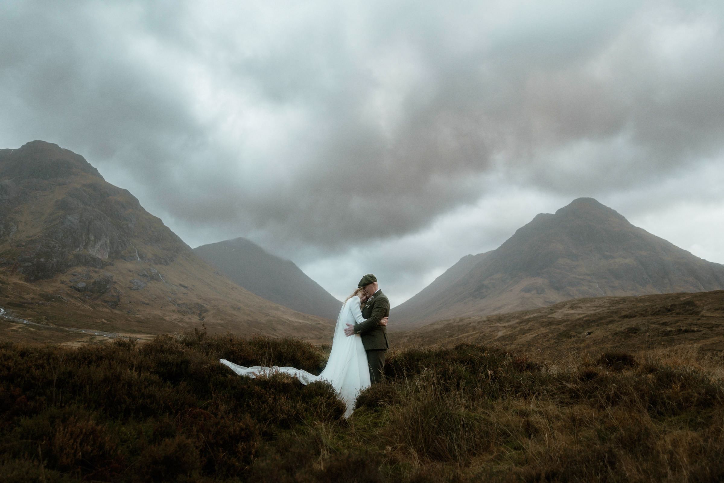 A bride and groom hold each other on their elopement day with the mountains of Glencoe behind them in Scotland